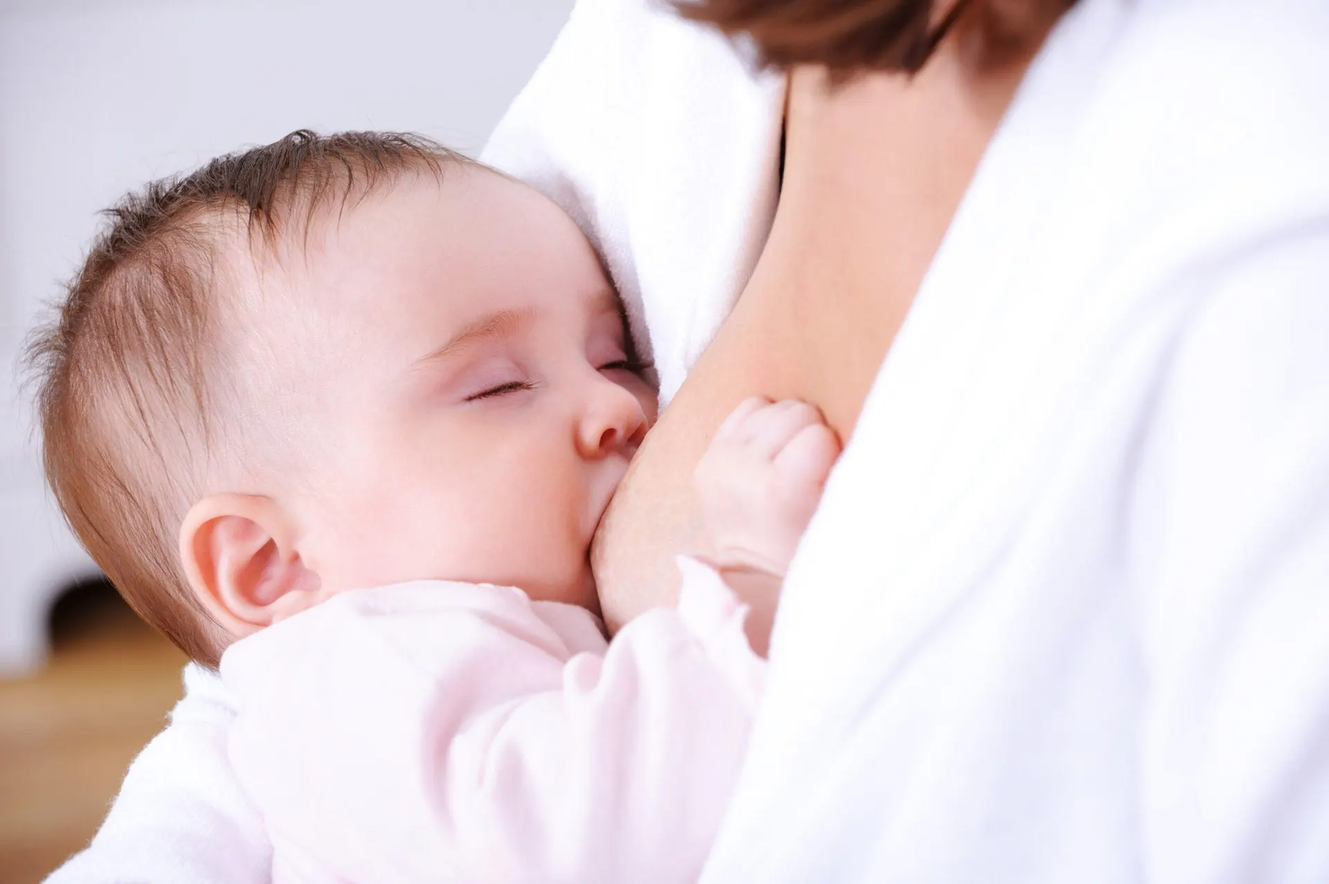 A mother feeding her baby, held close and settled